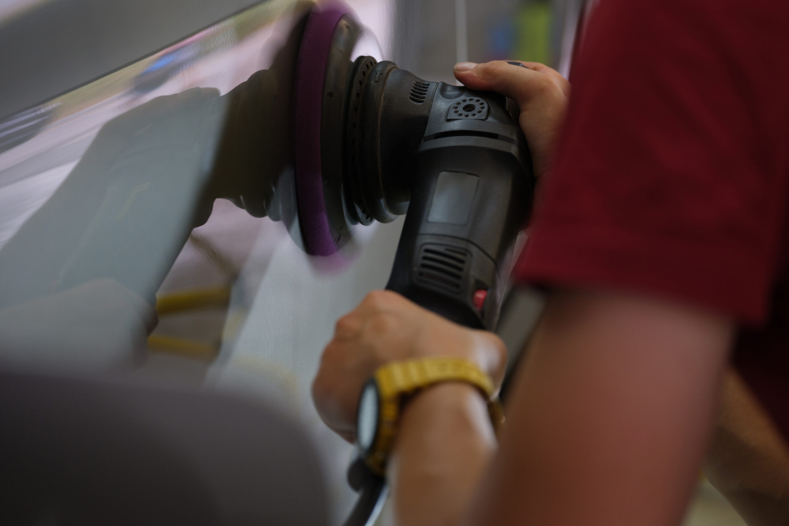 A technician polishing a vehicle panel with a dual-action buffer to restore the paint finish.