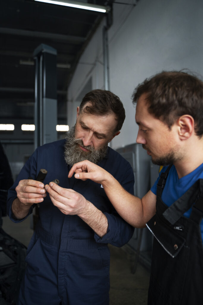 Two automotive technicians inspecting and discussing a vehicle component in a workshop.