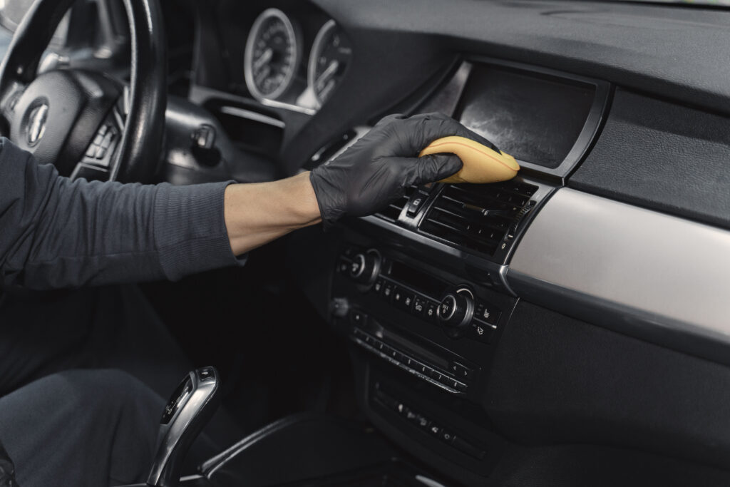Technician cleaning a car dashboard and centre console with a sponge during an interior detailing service.