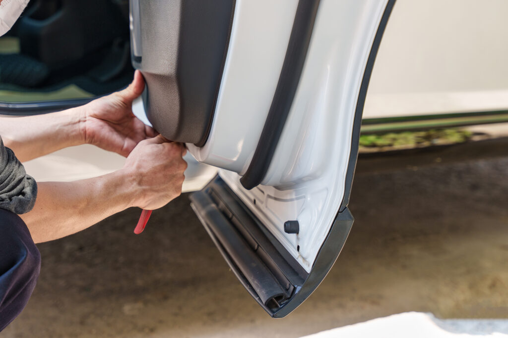 Technician removing an interior door trim panel from a vehicle for repair or inspection.