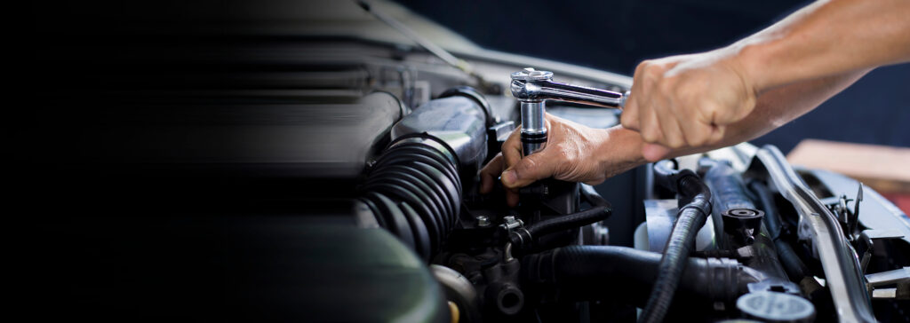 A mechanic uses a ratchet wrench to repair an engine inside a vehicle's engine bay.